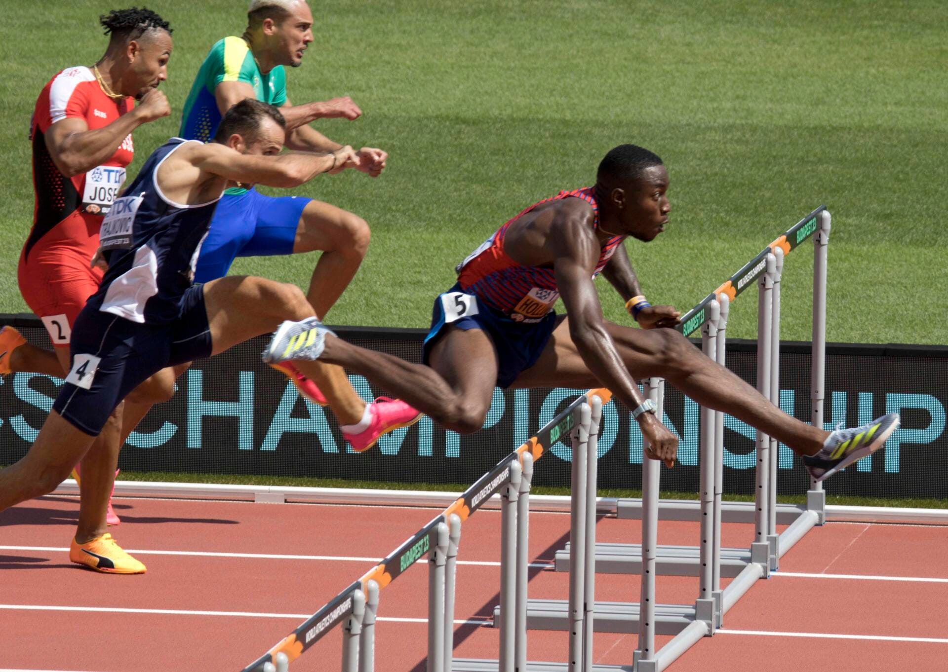 Grant Holloway clearing a hurdle in the USA vest during the 110 m hurdles heats at the 2023 World Championships in Budapest