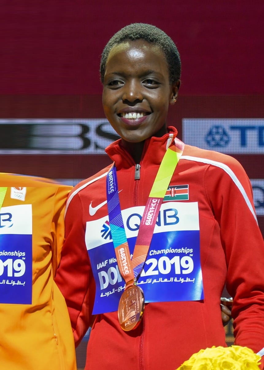 Agnes Tirop on the podium of the women's 10,000 metres at the 2019 World Athletics Championships in Doha, wearing her bronze medal and the Kenyan team jacket